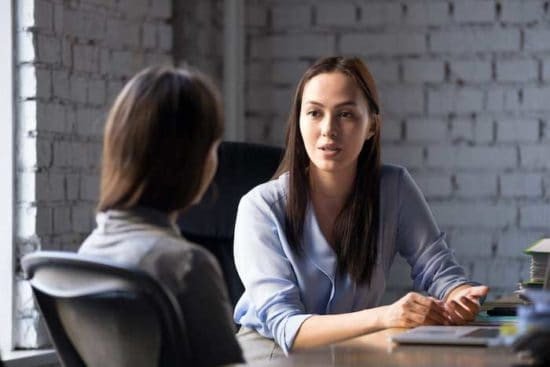 Hai người phụ nữ tham khảo ý kiến bên bức tường gạch đang ngồi ở bàn, hình ảnh tư vấn pháp lý cho người tị nạn
