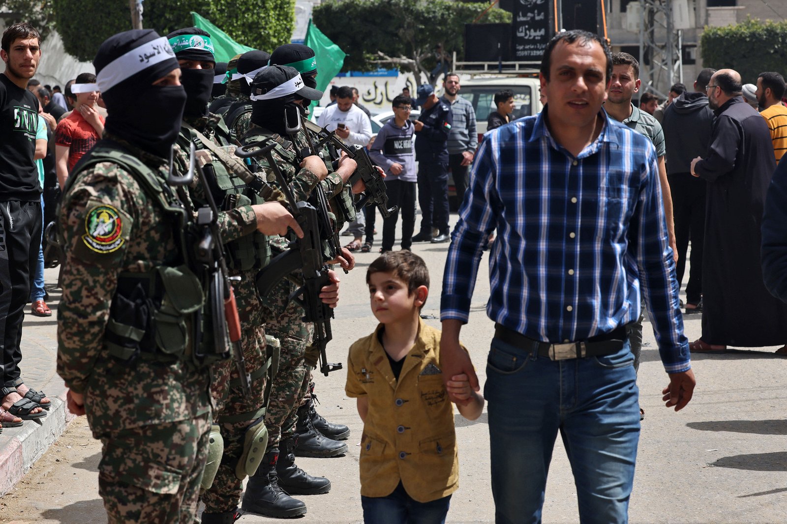 Một người đàn ông Palestine cùng con trai đi qua các thành viên Hamas ở Dải Gaza, liên quan đến câu hỏi Hamas là nước nào
